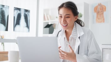 A female clinician in her office smiles while looking at a laptop during a patient telehealth visit
