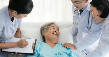 An elderly woman laying in a hospital bed is surrounded by her care team as she prepares to transition home