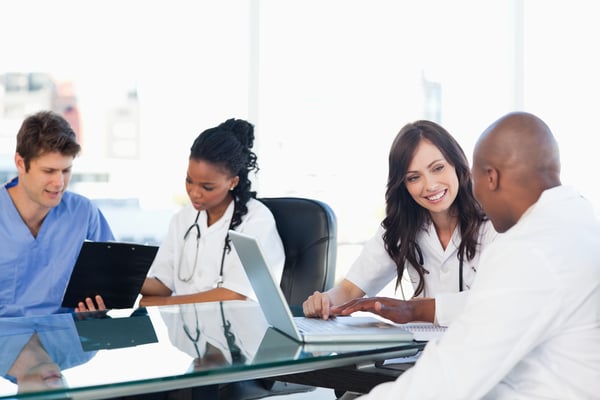 Smiling medical team working both on a laptop and a clipboard