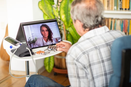 Elderly man with blood pressure cuff and medications using telehealth